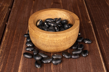 Lot of whole black bean in bamboo bowl on brown wood