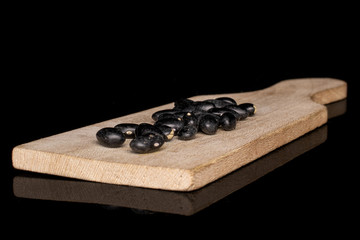 Lot of whole black bean on wooden cutting board isolated on black glass