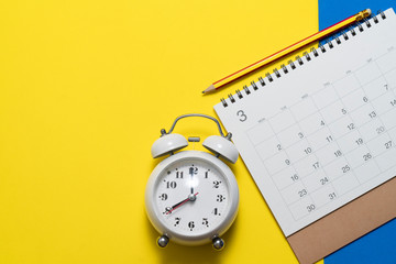 close up of calendar and alarm clock on the yellow table background, planning for business meeting or travel planning concept