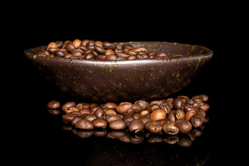 Lot of whole fresh coffee bean in glazed bowl isolated on black glass