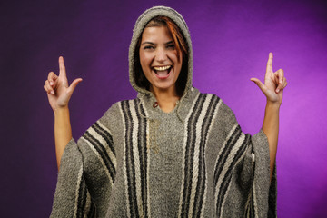 Ragazza con poncho , giocando divertita , fa il segno delle pistole  con le dita, isolata su sfondo...