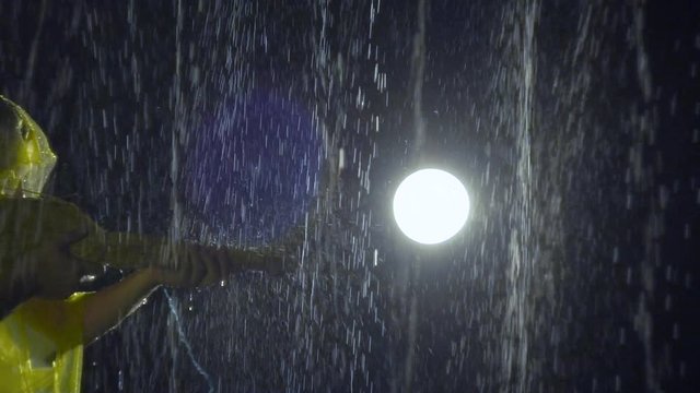 Man with broom and raincoat is walking, as if with weapon rifle gun in his hands in rain. One in yellow slicker with besom like a military soldier is fooling around and playing war games. Water drips
