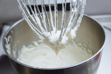 Process of cooking meringue. Whipped egg whites on mixer whisk on linen towel over gray texture...