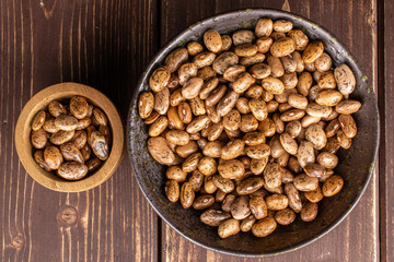 Lot of whole mottled brown bean pinto in glazed bowl in bamboo bowl flatlay on brown wood