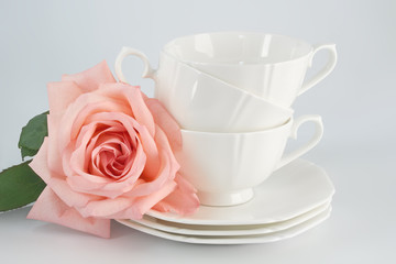 Fototapeta na wymiar White porcelain cup with a saucer for tea or coffee and pink rose, demitasse or teacup. Crockery on white background.