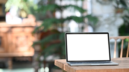 Photo of computer laptop with white blank screen putting outdoors on the modern table with classic cafe as background.