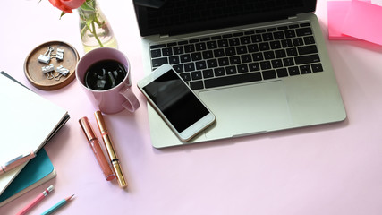 Top view of woman table with accessories and woman cosmetic putting on it. Computer laptop, smartphone, post-it, coffee cup, cosmetic, notebook, clip and potted plant Flat lay together on pink table.