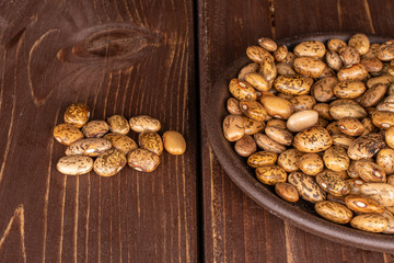 Lot of whole mottled brown bean pinto with brown ceramic coaster on brown wood