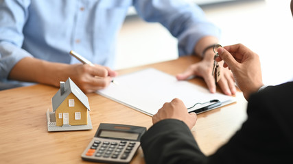 Cropped shot of House broker giving a property key to his customer while he has writing/signing on...