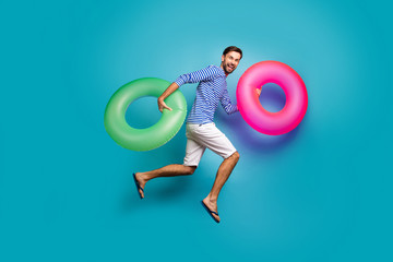 Full length photo of funky crazy guy tourist jump high running swimming hold two colorful lifebuoys...