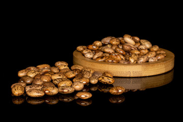 Lot of whole light mottled brown bean pinto on round bamboo coaster isolated on black glass