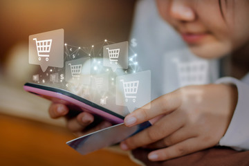 Young woman holding credit card while using mobile phone to buying products on ecommerce. Shopping cart balloon and network wire floating on smartphone hold by hand. Ecommerce and online marketing.