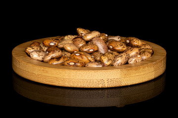 Lot of whole mottled brown bean pinto on round bamboo coaster isolated on black glass