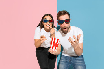 Obraz premium Watching 3D-cinema with popcorn. Young and happy man and woman in casual clothes on pink, blue bicolored background. Concept of human emotions, facial expession, relations, ad. Beautiful couple.