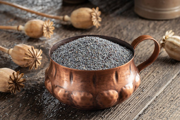 Poppy seeds in a cup with poppy pods in the background