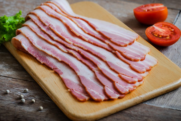 Raw sliced bacon on wooden board