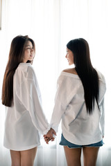 Two women holding hand  and looking each other with sweet emotion,beside window,feeling loved,romantic love couple,good friendship,blurry light around