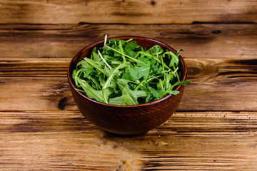 Ceramic bowl with arugula leaves on wooden table
