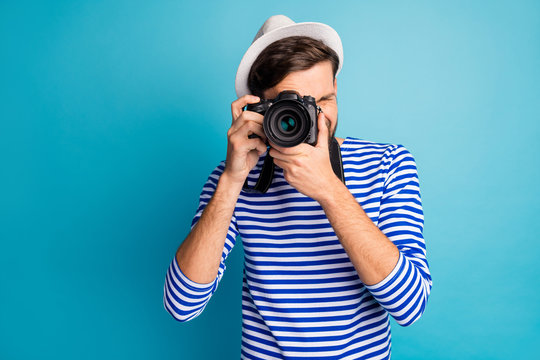 Photo of attractive guy photographer hold professional digital lens camera traveler make view pictures wear striped sailor shirt vest white cap isolated blue color background