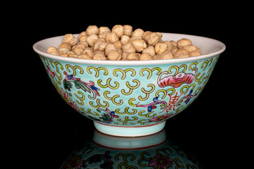 Lot of whole fresh tan chickpea with blue chinese ceramic bowl isolated on black glass
