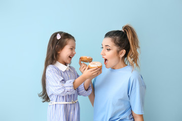 Beautiful young woman and little girl eating donuts on color background