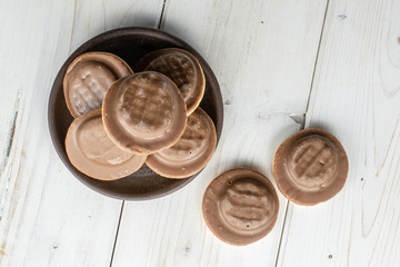 Group of seven whole chocolate biscuit with brown ceramic coaster flatlay on white wood
