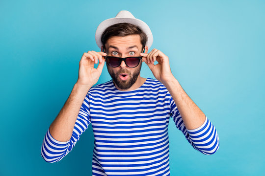 Photo of funky excited handsome guy tourist taking off cool black sun specs open mouth read discounts banner wear striped sailor shirt cap isolated blue color background