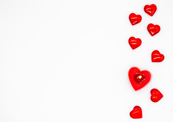 A red burning candle in the shape of a heart and few glass hearts are lying on a row on the left. Concept of love, Valentine's day, passion. Copy space