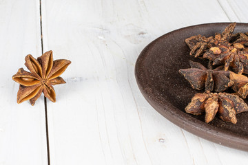 Lot of whole aromatic brown badian with brown ceramic coaster on white wood