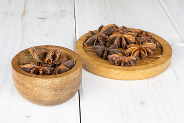 Lot of whole aromatic brown badian on round bamboo coaster in bamboo bowl on white wood