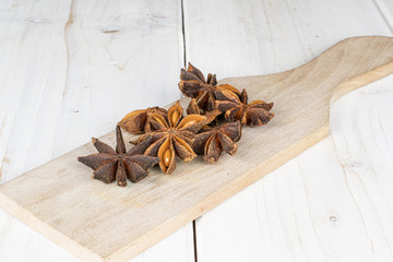 Lot of whole aromatic brown badian on wooden cutting board on white wood