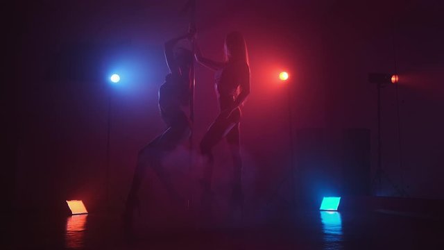 Beautiful dancing girls with sexy body pole dancing in slow motion. Two silhouettes at red and blue background. Full length shot in 4K, UHD