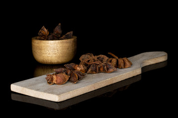 Lot of whole aromatic brown badian on wooden cutting board in bamboo bowl isolated on black glass