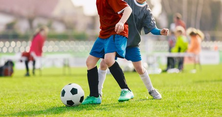 Obraz premium Youth Football Tournament. Youth Players Kicking Soccer Match on grass Stadium. Two Junior Level Soccer Players Compete for Ball in Red and Grey Shirts Compete for Ball