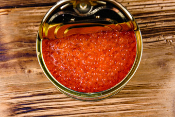 Metal tin can with red caviar on a wooden table. Top view