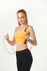 beautiful young slim woman with red hair in sportswear on a white background with a skipping rope in hands