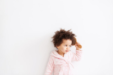 Cute little girl in soft bathrobe brushing her curly hair