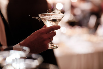A close up of a man's hand who is dressed in formal attire and holding a martini glass on party background.