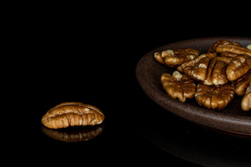 Lot of whole tasty brown pecan half with brown ceramic coaster isolated on black glass