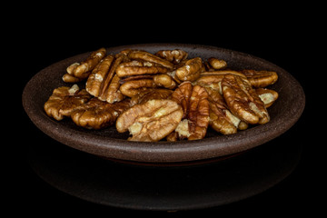 Lot of whole tasty brown pecan half with brown ceramic coaster isolated on black glass