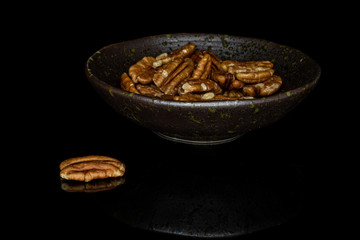 Lot of whole tasty brown pecan half in glazed bowl isolated on black glass