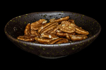 Lot of whole tasty brown pecan half in glazed bowl isolated on black glass