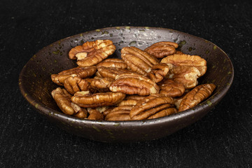 Lot of whole tasty brown pecan half in glazed bowl on grey stone