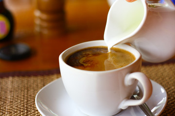 hand pouring milk to coffee cup on wood table background