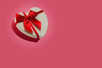 Above view on a heart-shaped gift box wrapped in a red bow on a pink background. Valentine's day concept. February 14th is love day. Place for text.