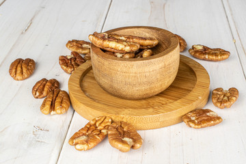Lot of whole tasty brown pecan half on round bamboo coaster in bamboo bowl on white wood