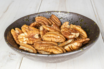 Lot of whole tasty brown pecan half in glazed bowl on white wood