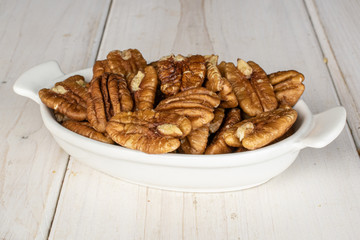 Lot of whole tasty brown pecan half on white ceramic plate on white wood