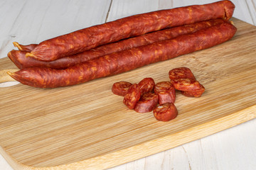 Group of four whole lot of slices of piquant smoked sausage on bamboo cutting board on white wood