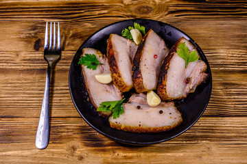 Slices of baked pork belly, garlic and parsley on a black plate